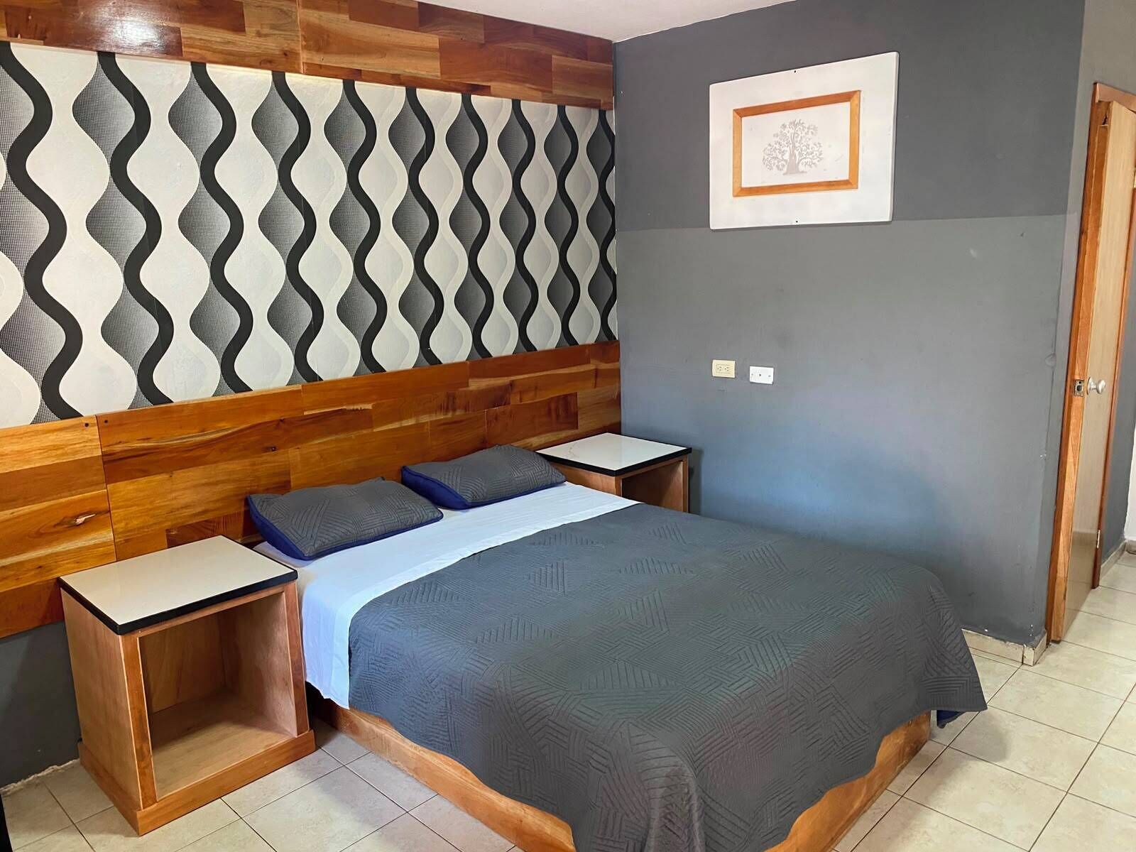 Une chambre à coucher avec un lit, deux tables de chevet, une tête de lit en bois, un mur à motifs et un tableau encadré accroché au mur.