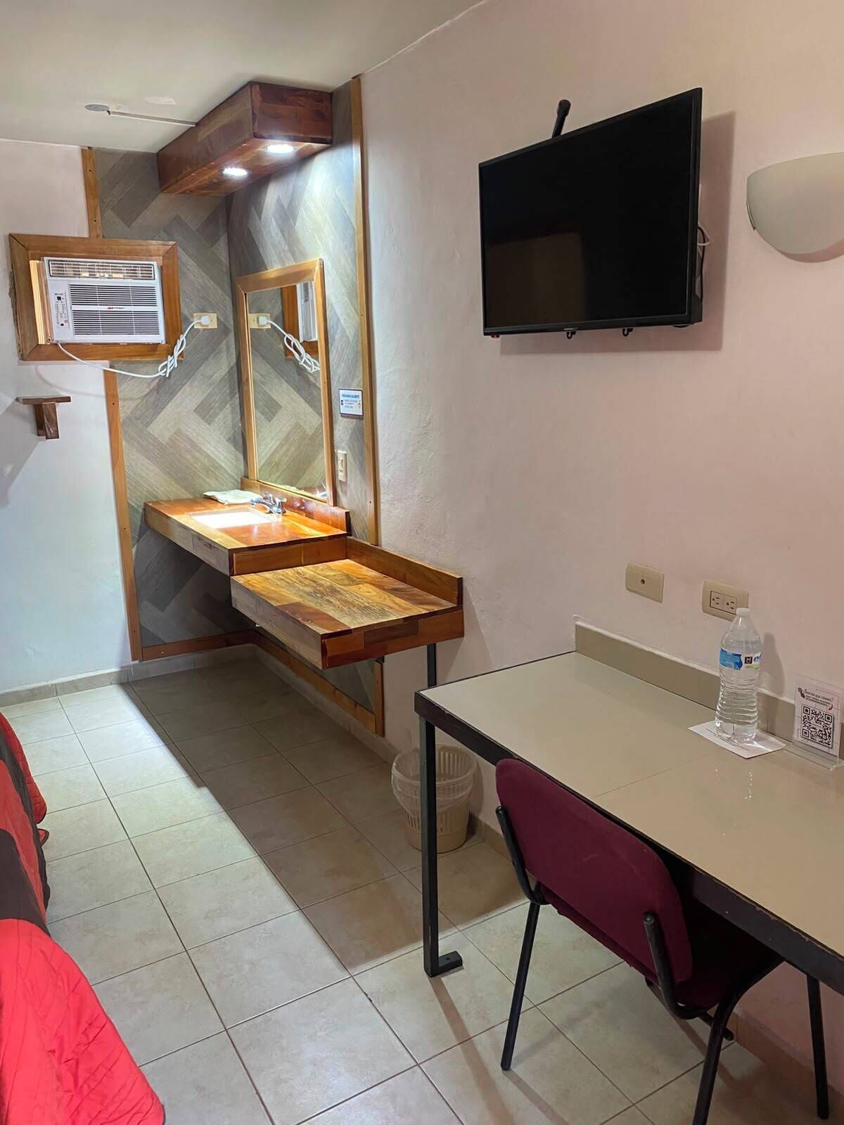 Habitación de hotel con tocador de madera, televisor montado en la pared, piso de baldosas y una silla roja.