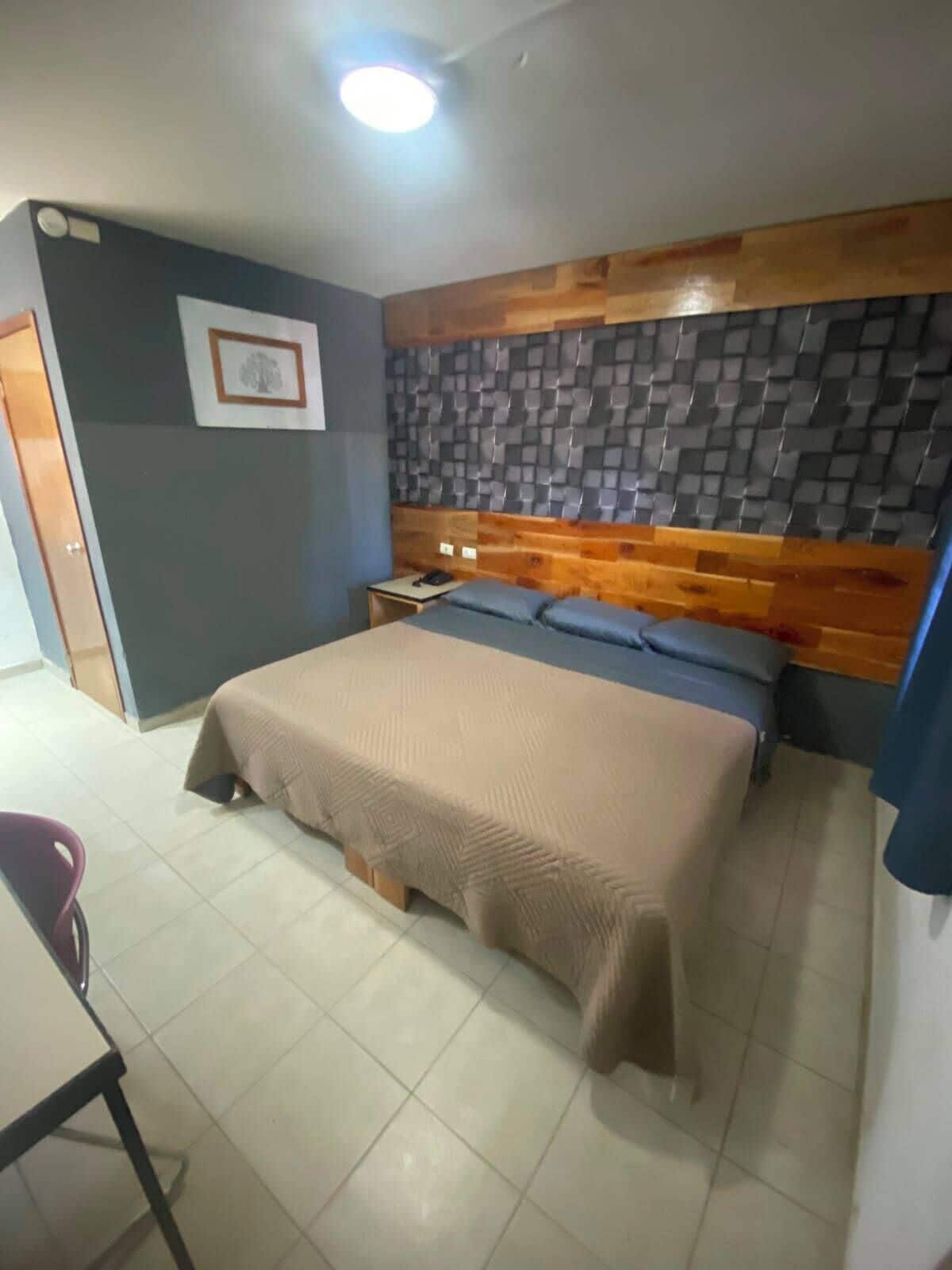 A bedroom with a bed, a nightstand, a chair, and a wall-mounted shelf.