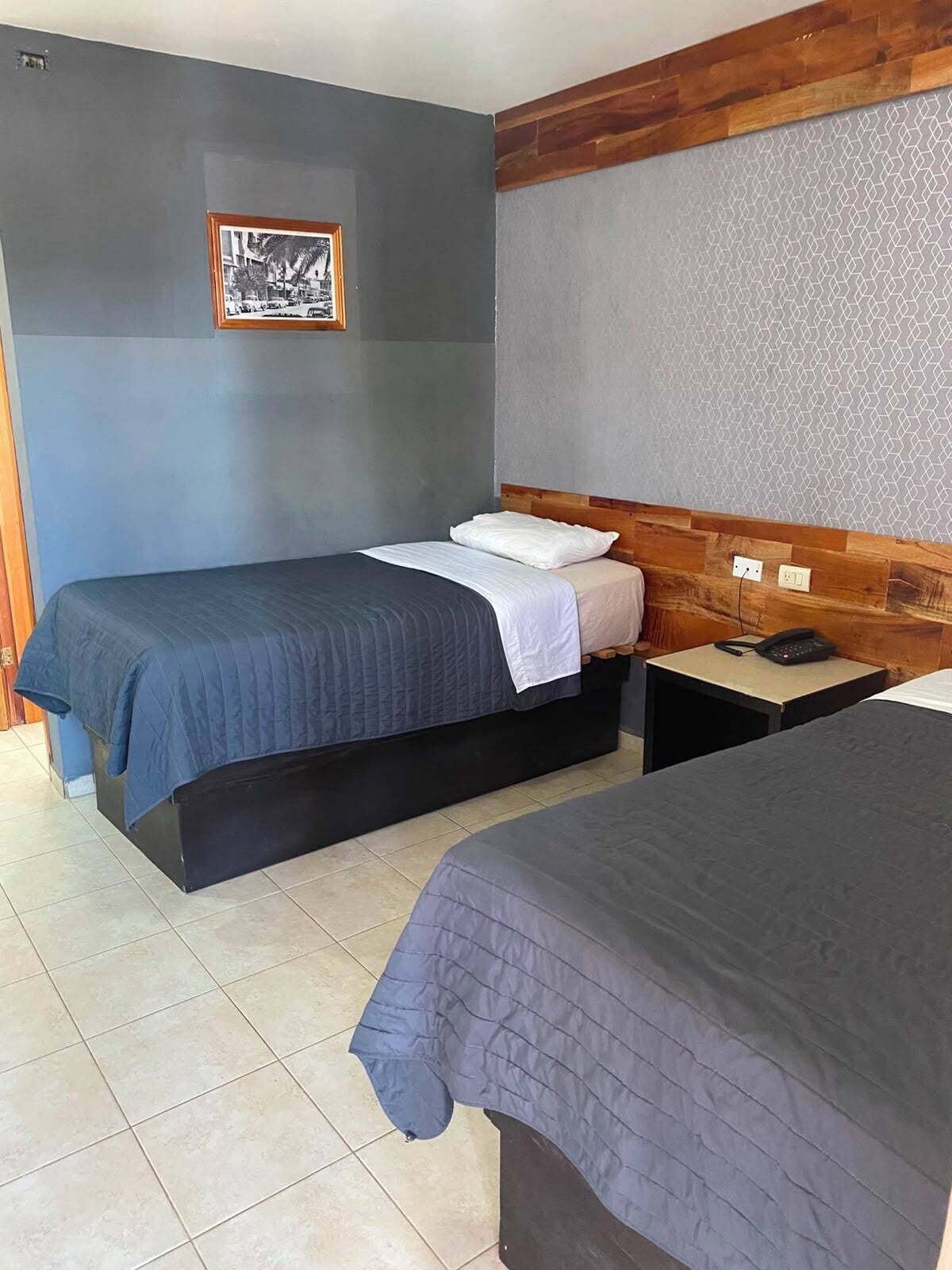 A room with two beds, a wooden headboard, a tiled floor, and a framed picture on the wall.