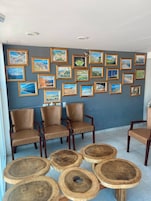 Una habitación con un muro de cuadros de paisajes, sillones de cuero y mesas redondas de madera.