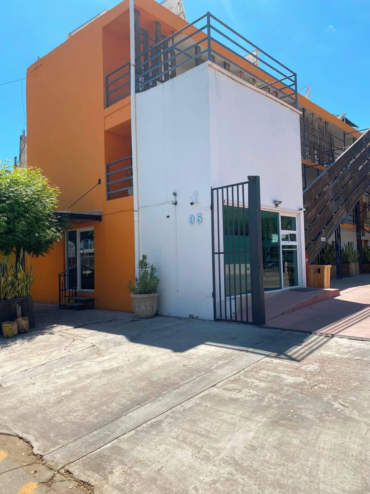 Um edifício de dois andares com fachada branca e laranja, uma entrada com portão e uma escadaria que leva ao nível superior.