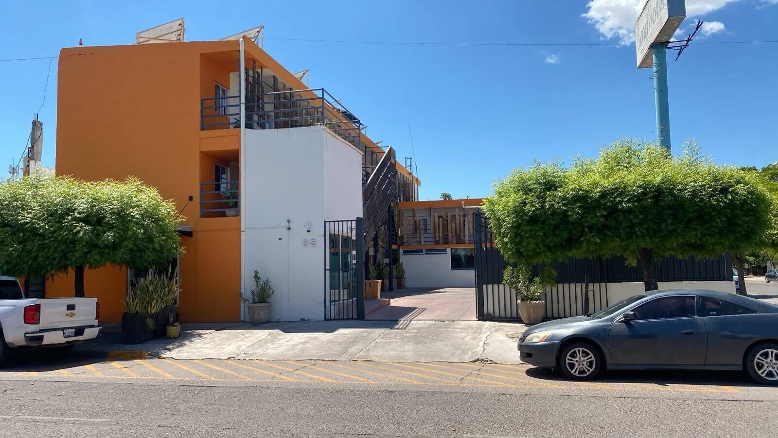 A residential building with a gated entrance, a parked truck, and a car on the street.