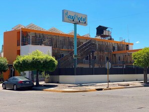 A MaxinHotel building with a sign, a staircase, and a parked car.