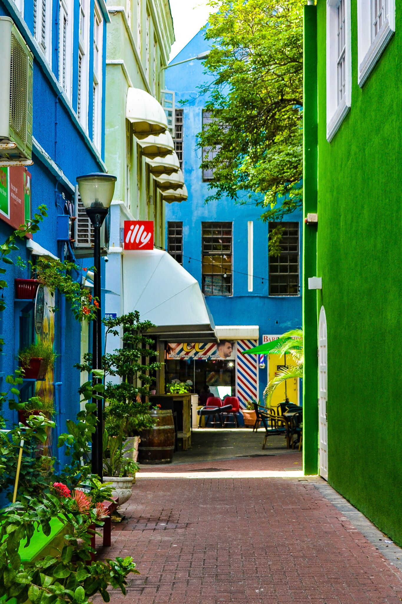 A narrow alley with a barber shop, a green building, and a blue building with a 'illy' sign.