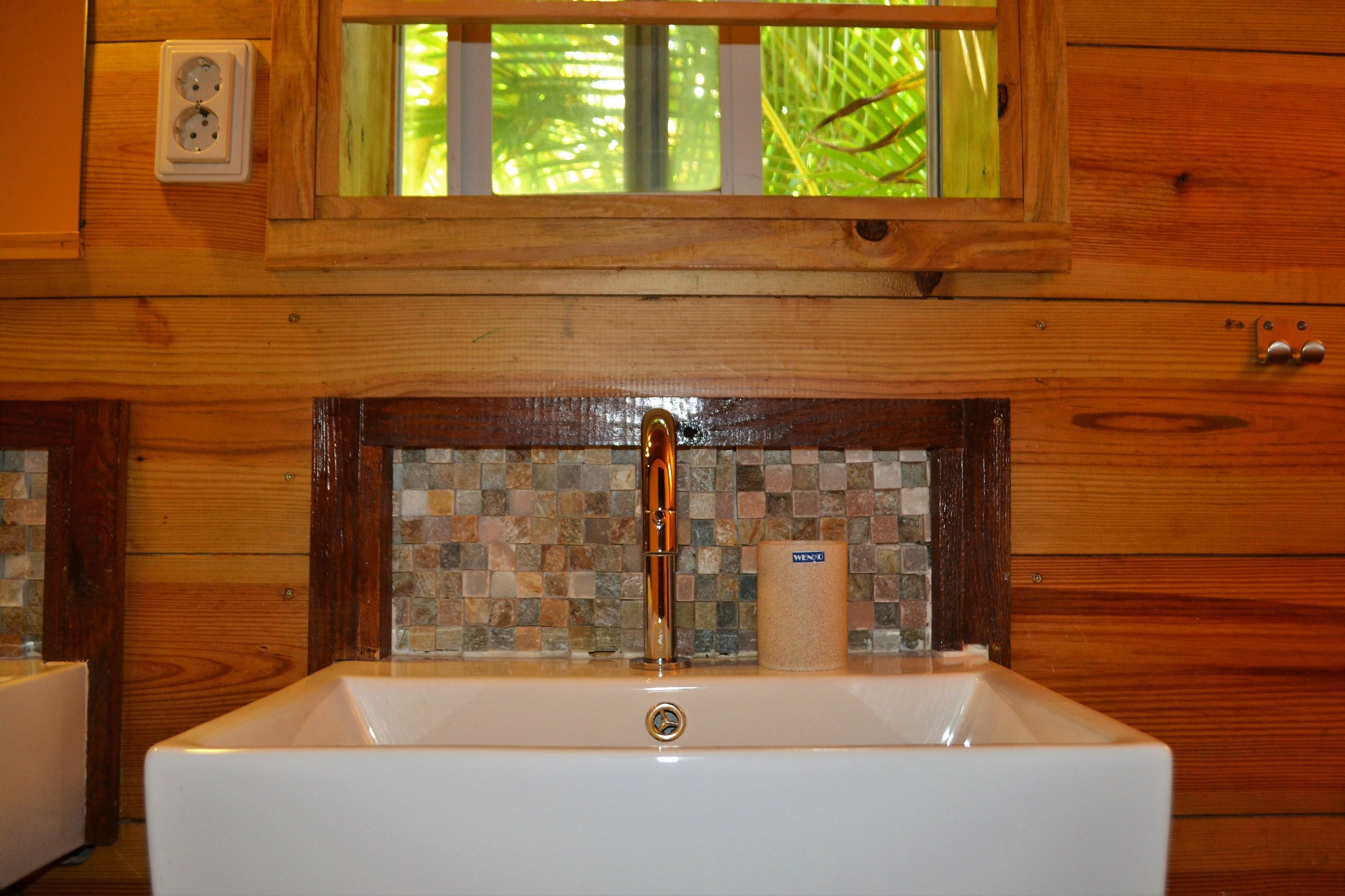 Un baño con lavamanos blanco, salpicadero de mosaicos y ventana sobre el lavamanos.