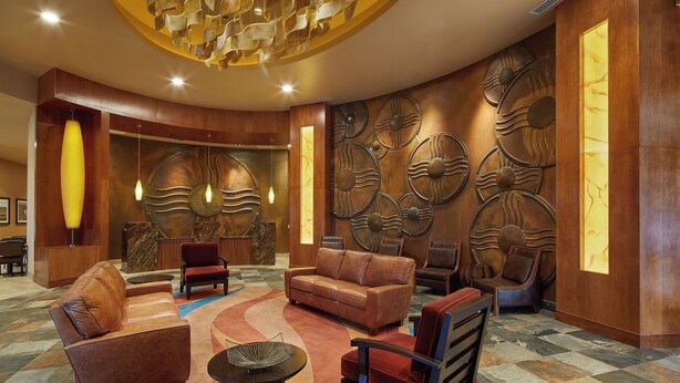 A lobby with a circular seating area, a reception desk, and a wall with decorative panels. - Zia Park Hotel (Hobbs)