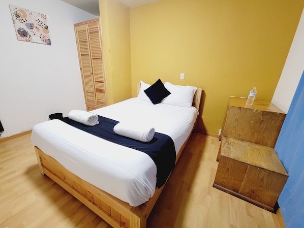 Ein ordentlich bezogenes Bett mit weißer und marineblauer Bettwäsche, ein Holz-Kopfteil und ein Nachttisch aus Holz mit einer Wasserflasche.