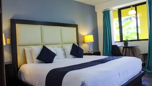 Una cama bien hecha con cabecera, lámpara de noche y ventana con cortinas.