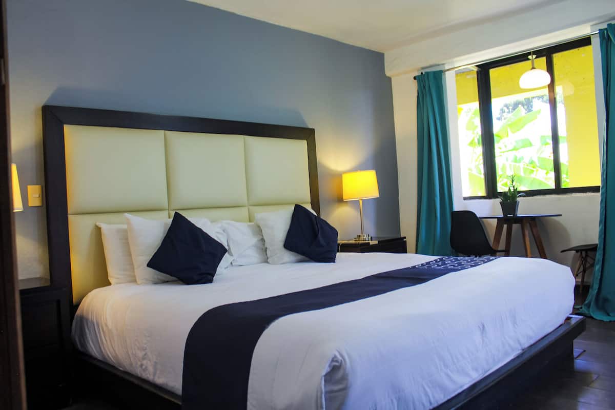 A neatly made bed with a headboard, a bedside lamp, and a window with curtains.