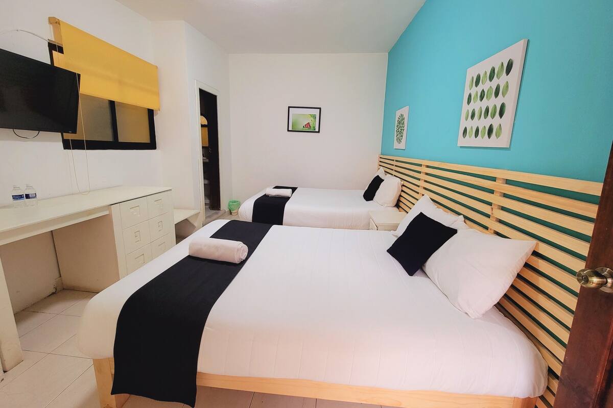 A hotel room with two beds, a desk, a TV, and artwork on the walls.