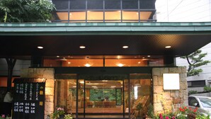 A building entrance with a glass door, potted plants, and a signboard. - Minamitei (Izumisano)
