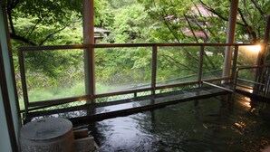 A traditional Japanese onsen with a view of lush greenery and a wooden structure. - Minamitei (Izumisano)