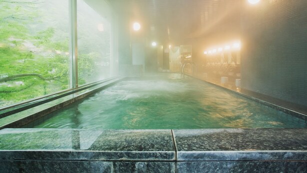 A hot spring bath area with a view of greenery outside, a tiled floor, and a row of lights along the wall. - Minamitei (Izumisano)