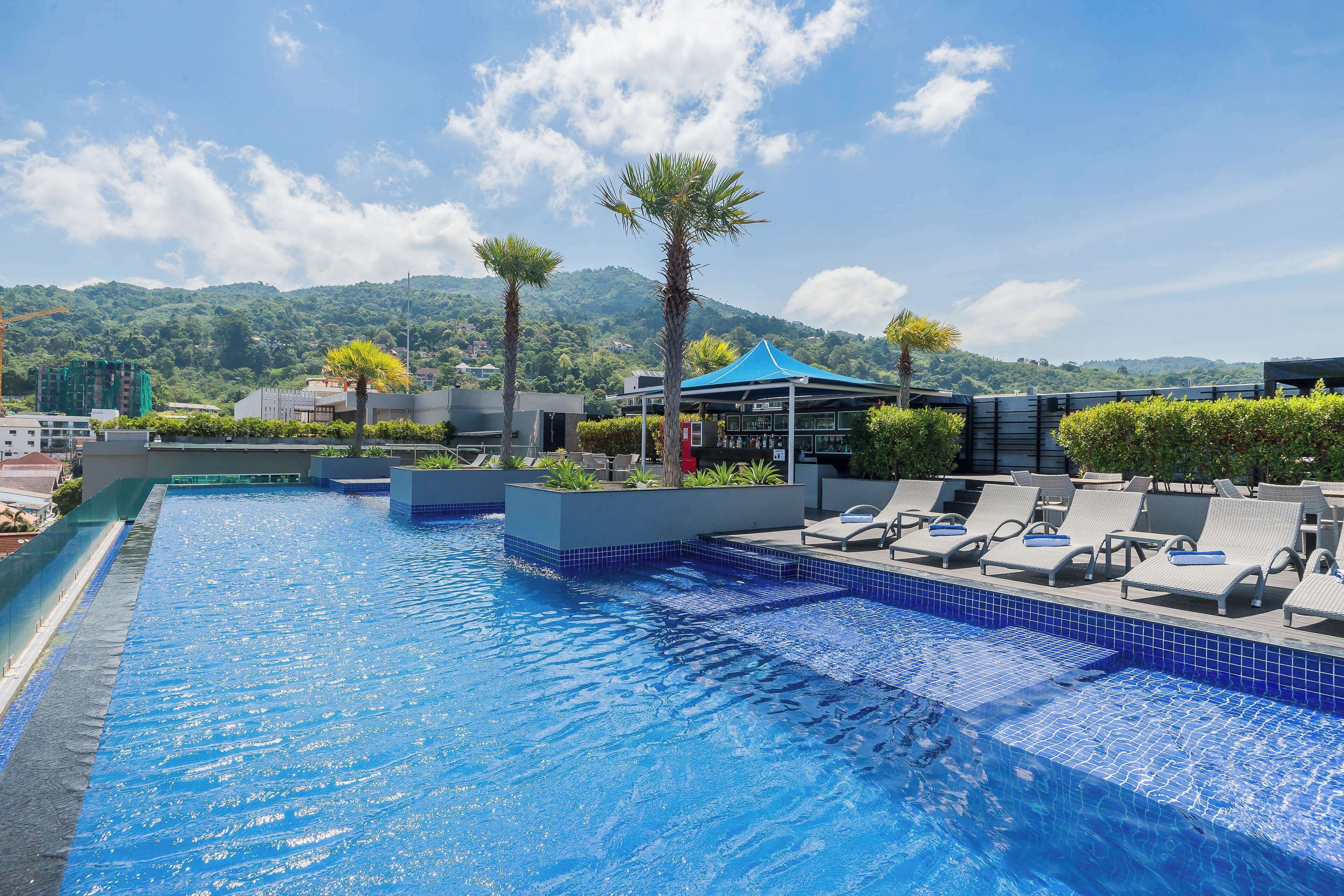A swimming pool with lounge chairs and a blue canopy, surrounded by greenery and mountains in the background.