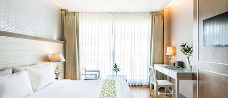 Hotellihuone, jossa on sänky, työpöytä, tuoli, televisio ja ikkuna, jossa on verhot.