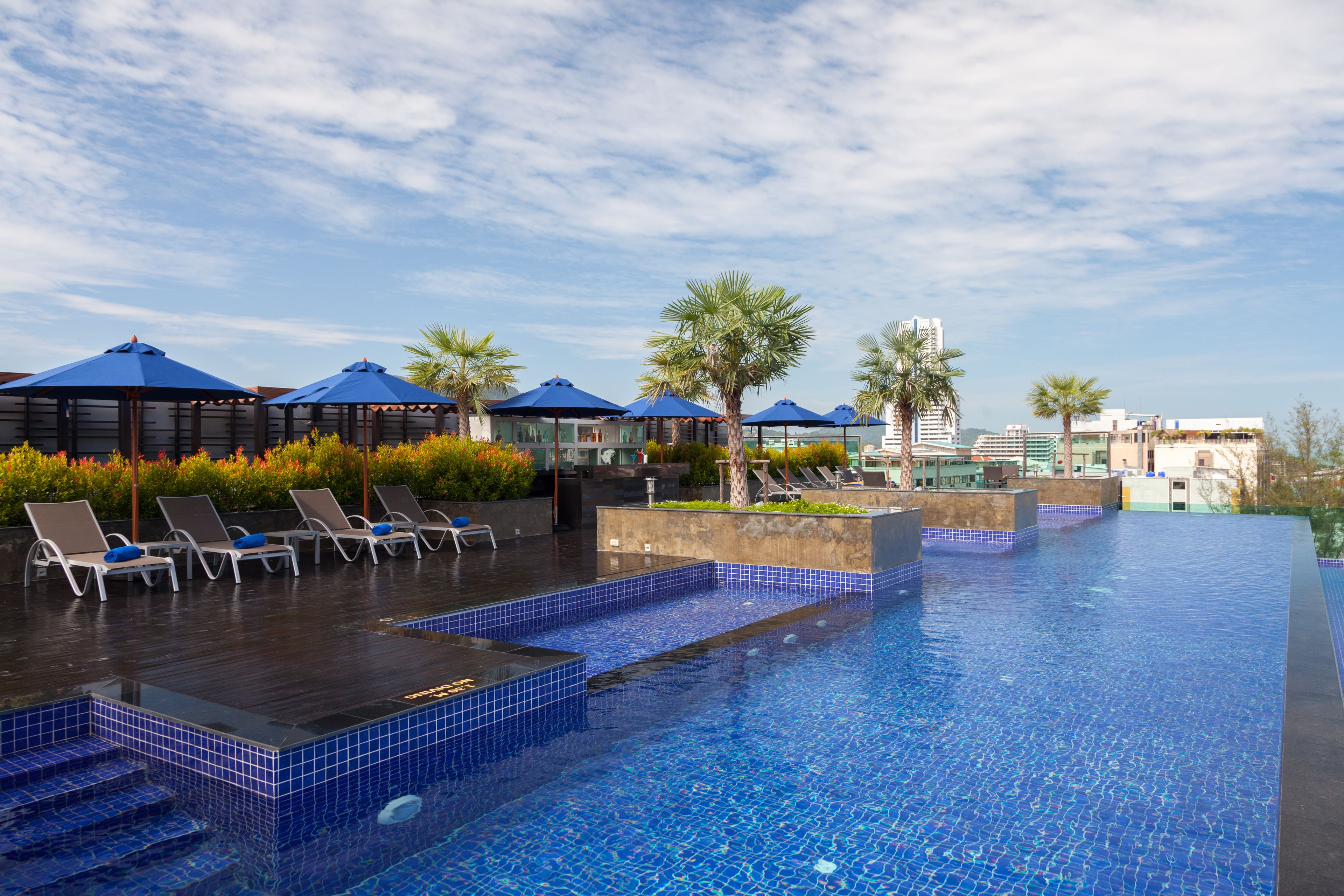 A swimming pool with blue-tiled steps and lounge chairs, surrounded by palm trees and blue umbrellas.