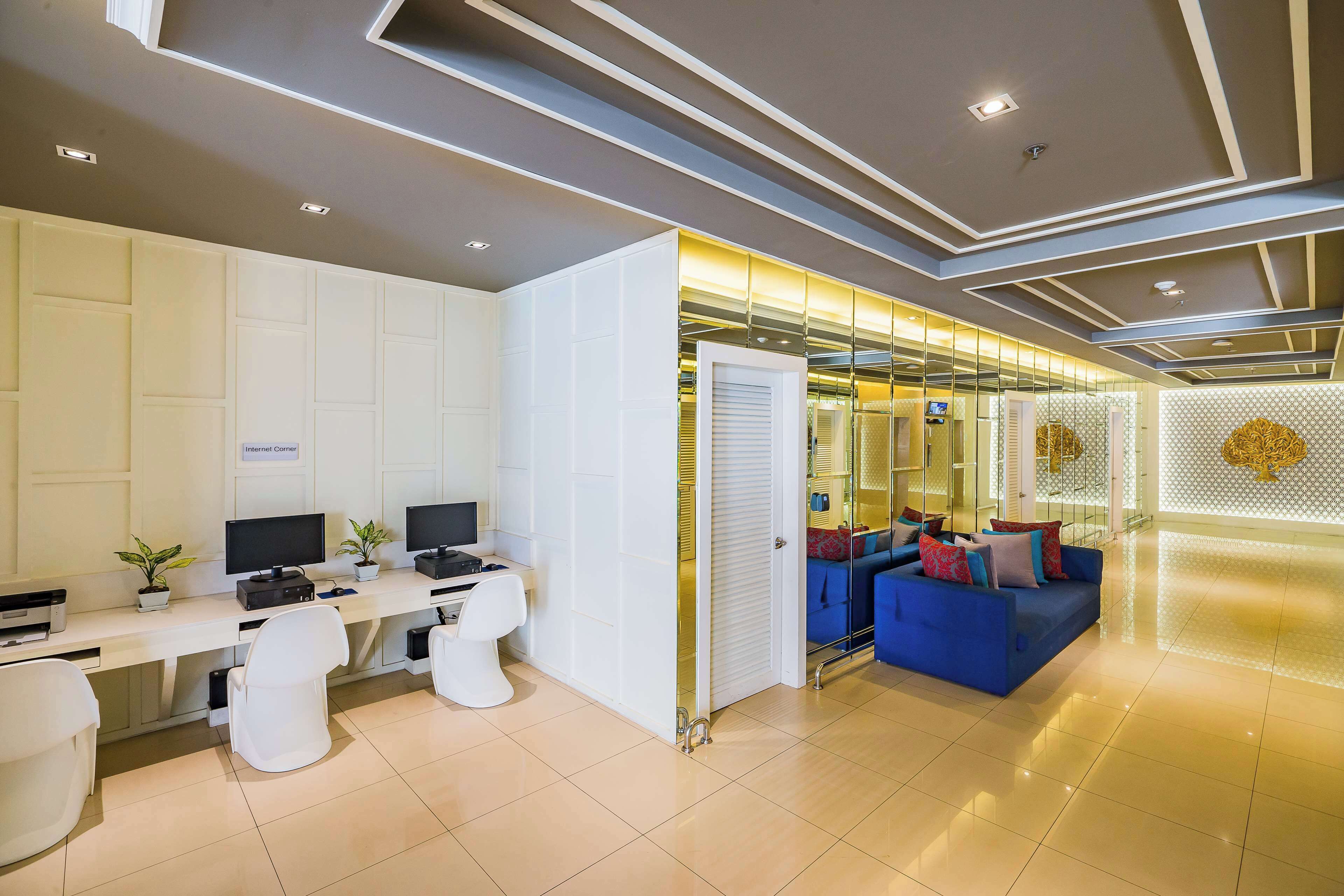 A modern hotel lobby with a reception desk, computers, seating area, and a decorative wall.
