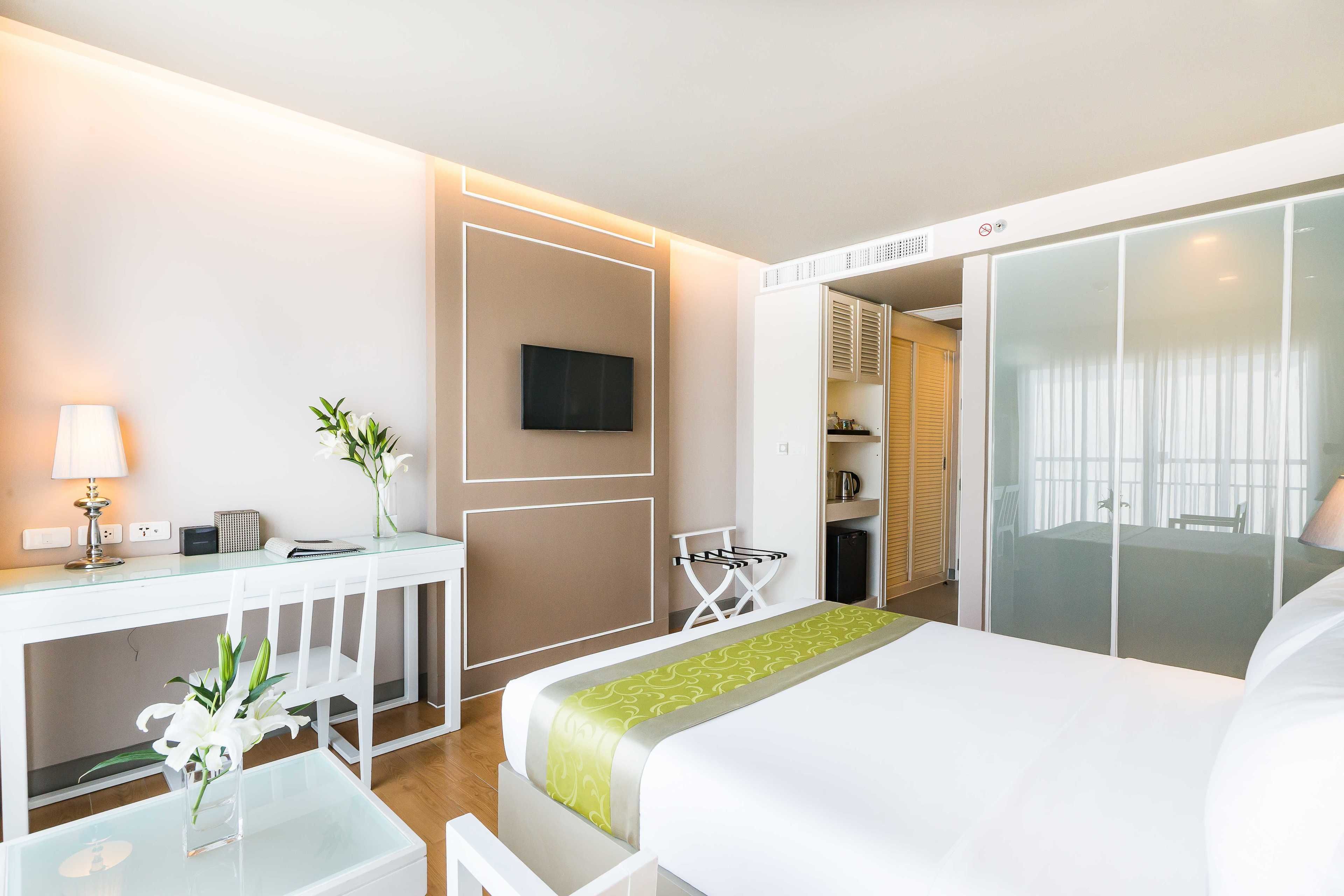 A hotel room with a bed, a desk with a lamp, a TV, and a sliding door to a bathroom.