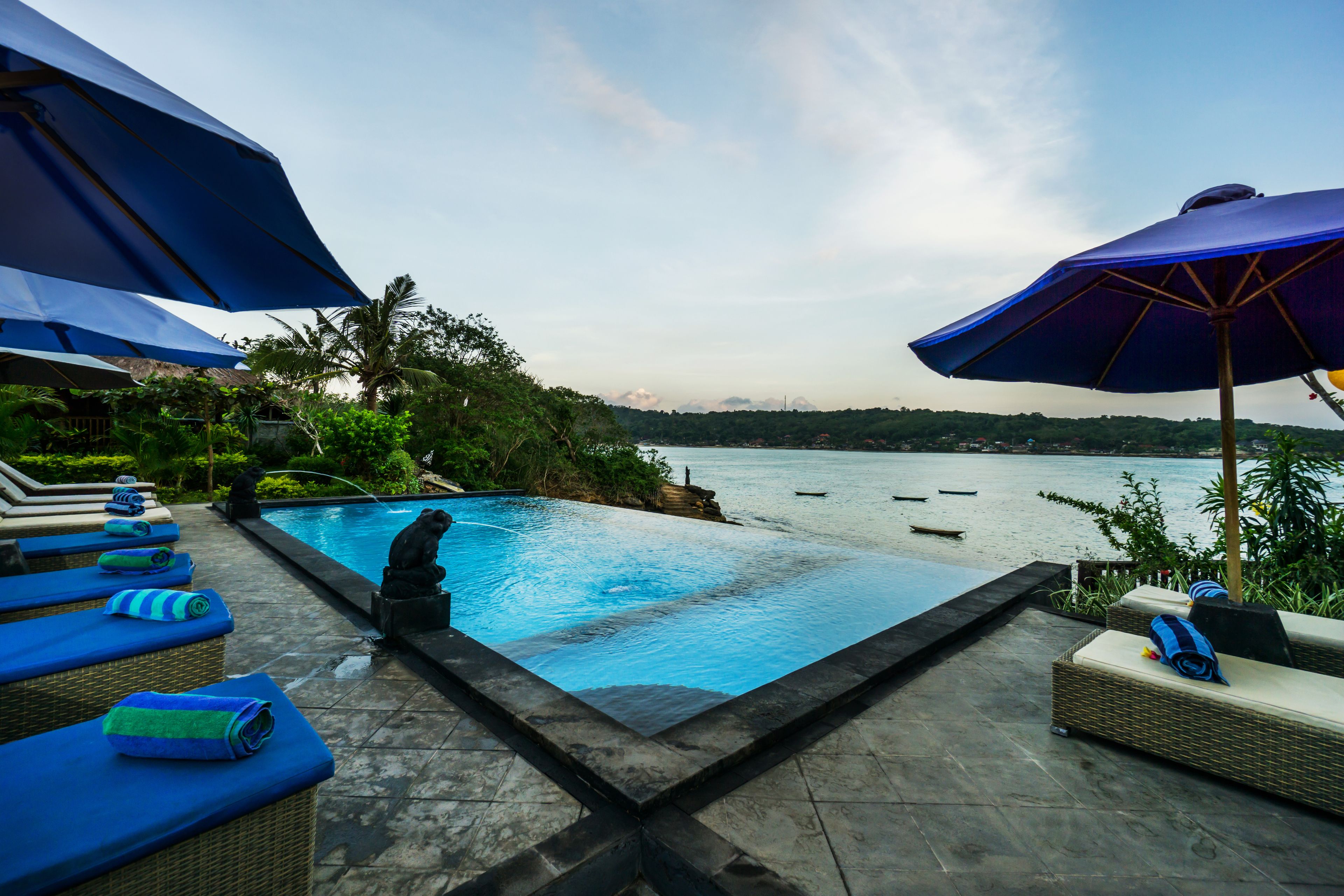 Un espace aménagé au bord de la piscine, avec des chaises longues et des parasols, donnant sur une étendue d’eau.