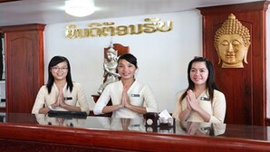 A reception desk with three staff members standing behind it, a Buddha statue, and a sign with Thai script. - Vansana Riverside Hotel (Vientiane)