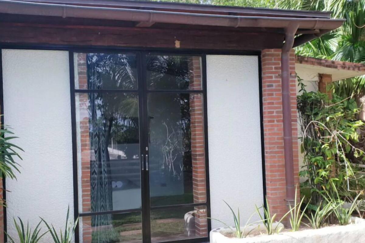 A glass door entrance with a brick wall, a small garden with plants, and a metal roof structure.