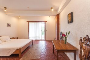 Un dormitorio con una cama, una mesa de madera con un florero y una puerta que da a un balcón.