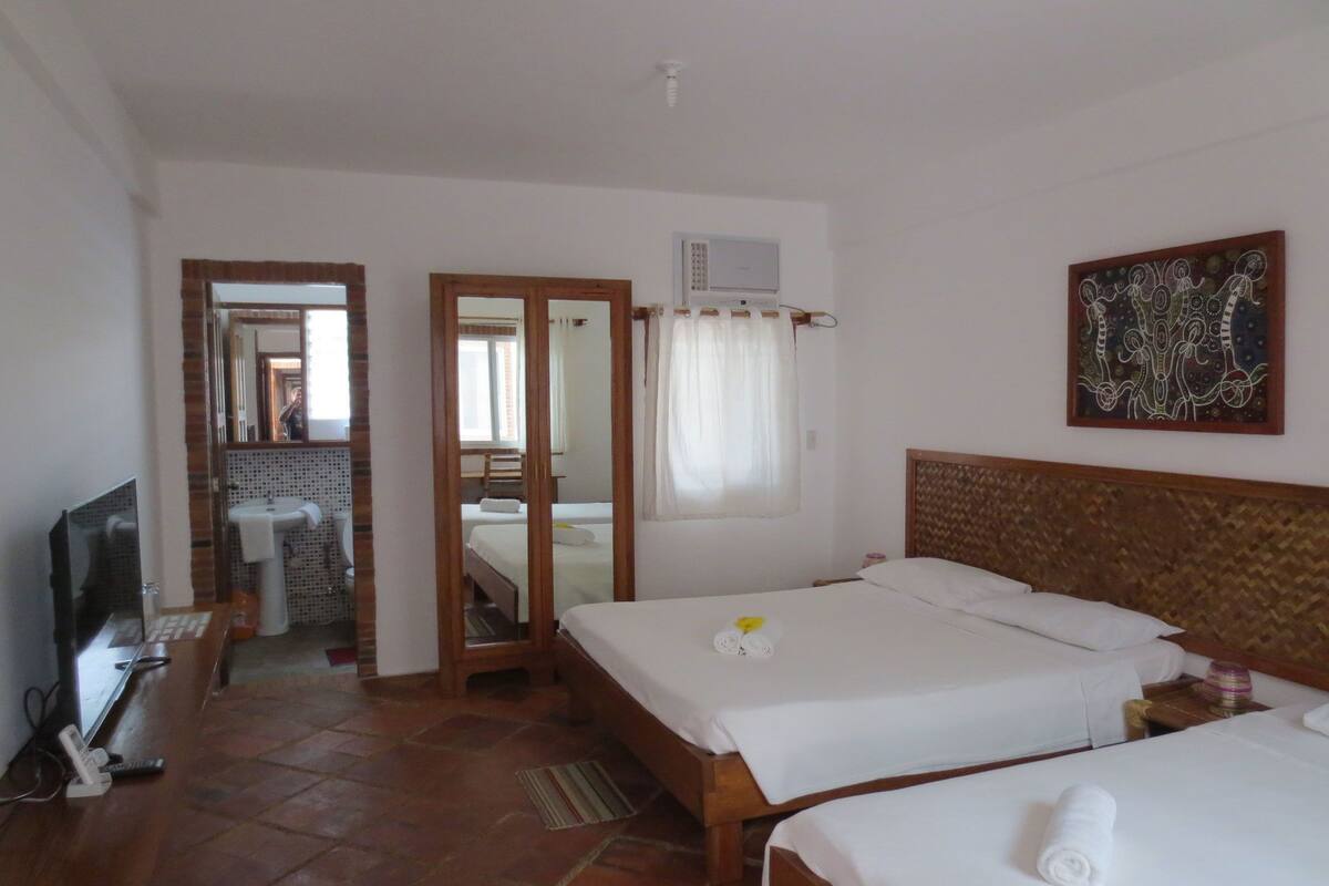 A hotel room with two beds, a television, a bathroom with a sink, and a mirror.
