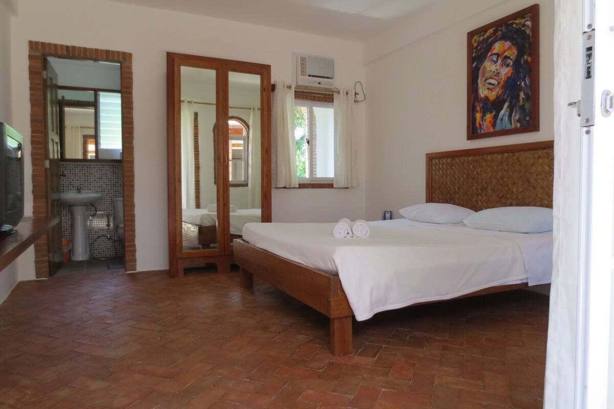 A bedroom with a wooden bed, a bathroom with a sink, and a large mirror.