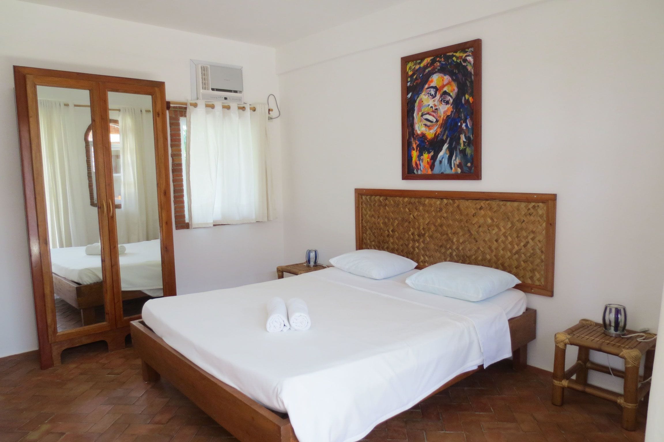 Une chambre d’hôtel avec un grand lit, une tête de lit en bois, une table de chevet, un miroir et un tableau au mur.