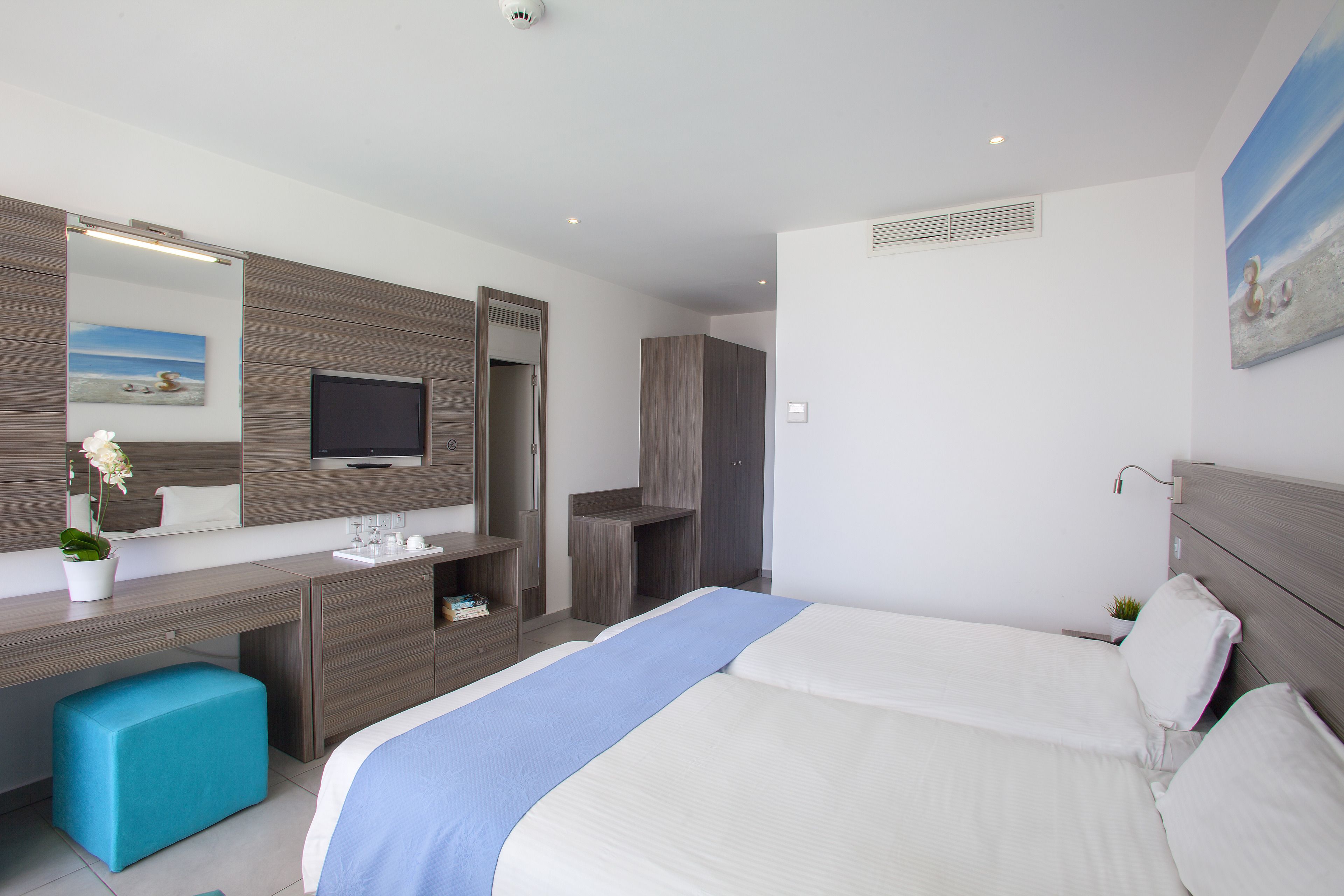 A modern hotel room with a large bed, a desk with a flat-screen TV, a bathroom, and a view of the sea.