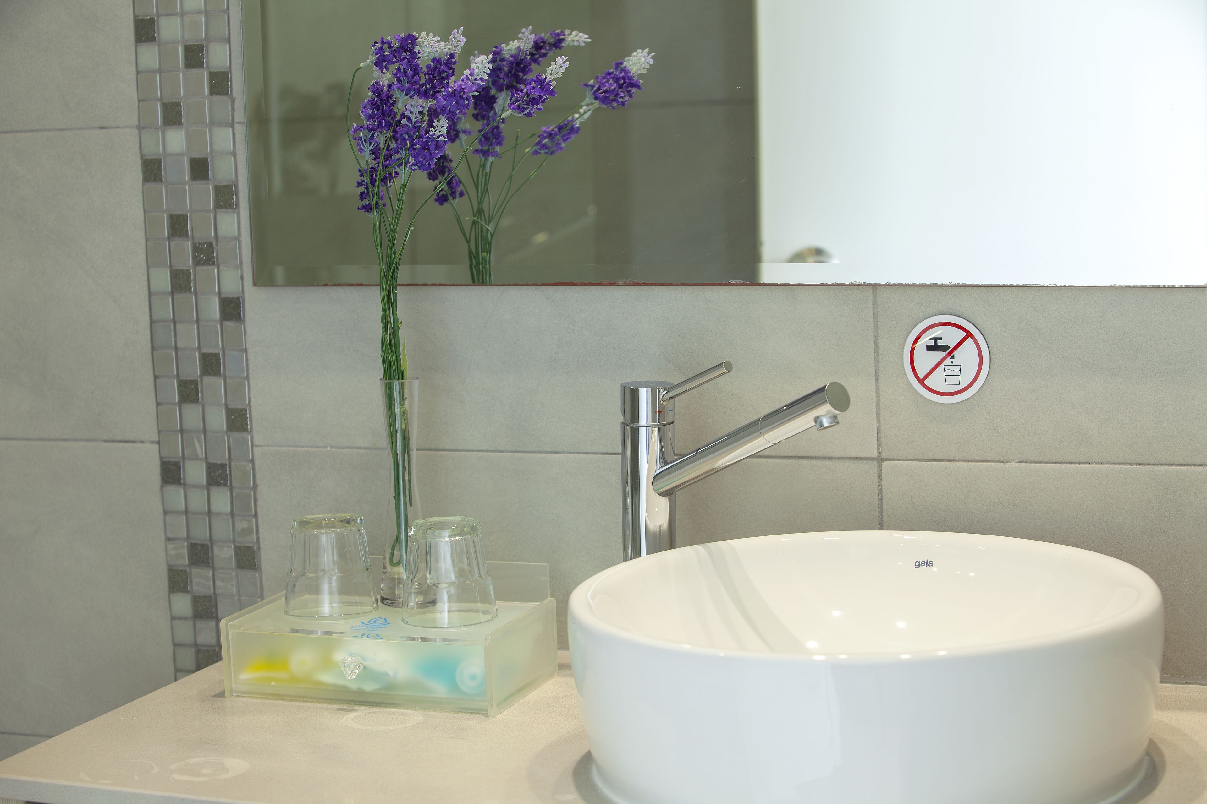 A bathroom with a white sink, a glass vase with purple flowers, and a no towel drying sign.