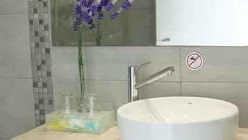 A bathroom with a white sink, a glass vase with purple flowers, and a no towel drying sign.