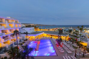 Un hotel con piscina en la azotea, varios balcones y vistas al mar.