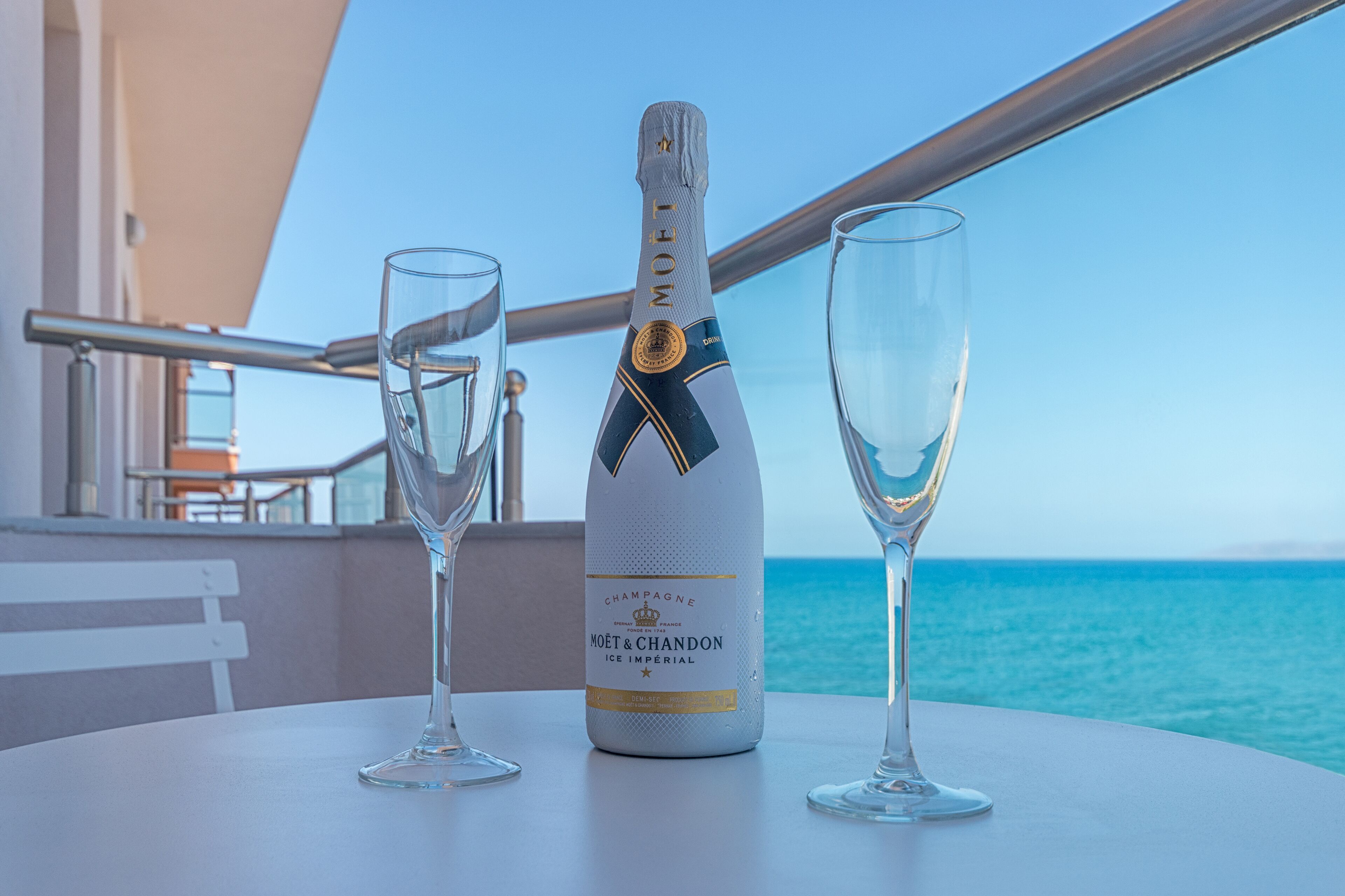 Una botella de Moët & Chandon Ice Imperial champagne sobre una mesa, con dos copas, con vista al mar.