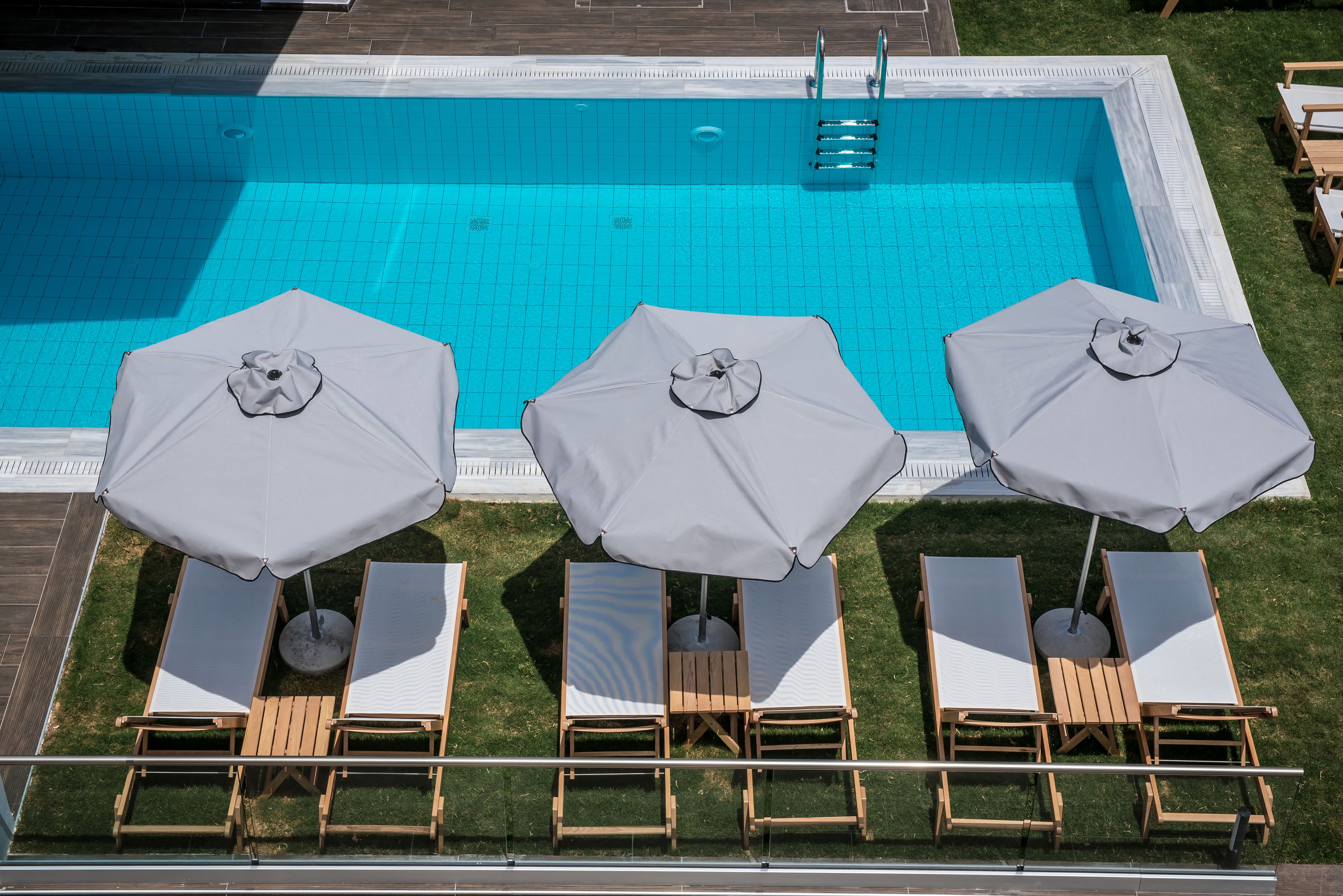 A swimming pool with three sun loungers and umbrellas, surrounded by a grassy area.