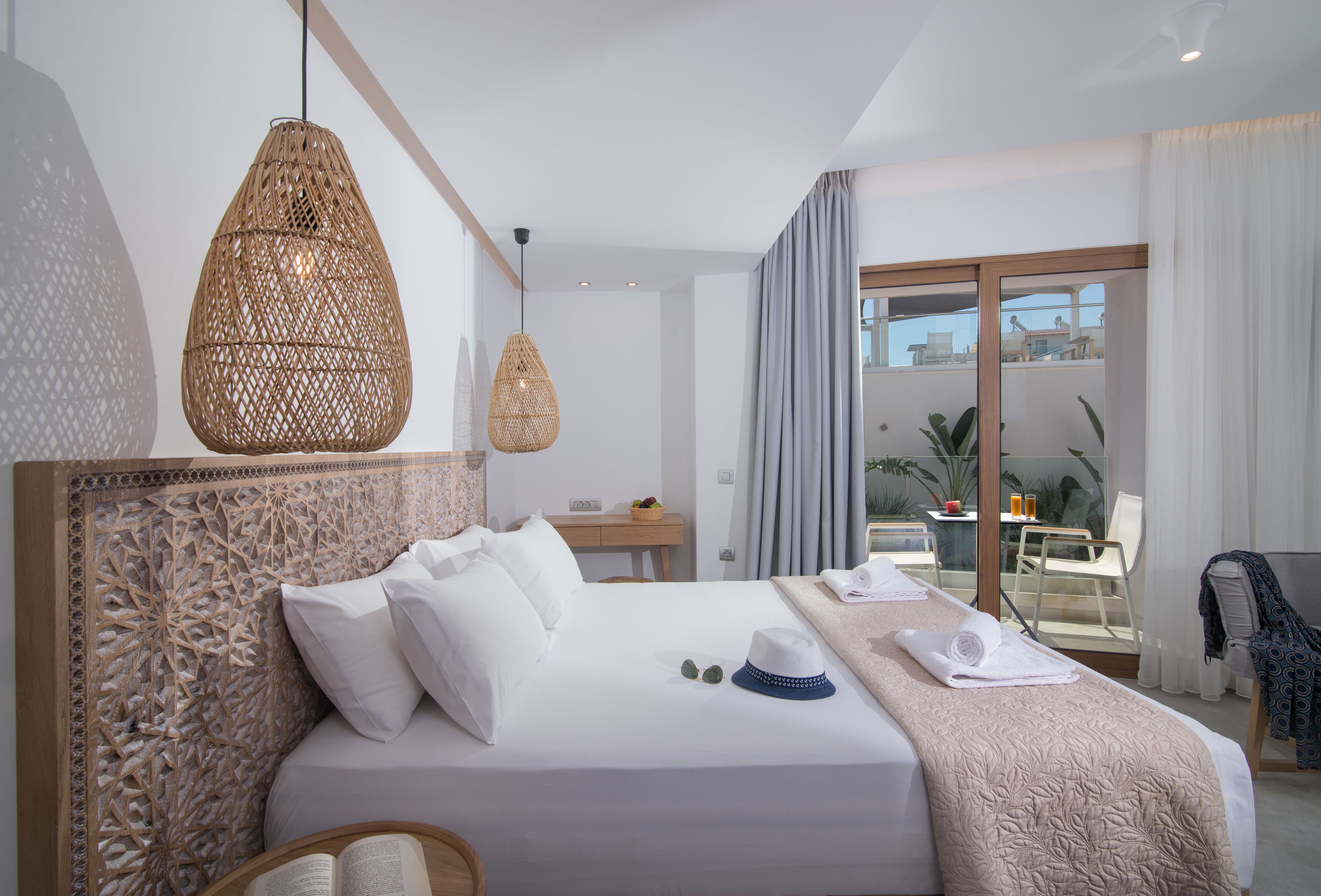 Habitación de hotel con una cama grande, cabecera de madera, zona de comedor con mesa y sillas, y balcón con vistas.