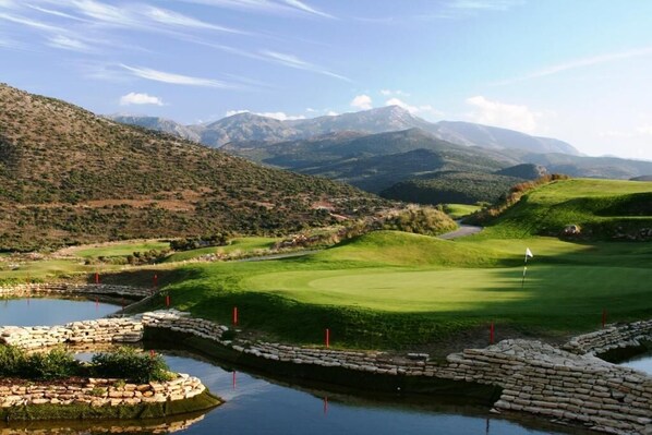 Un parcours de golf avec un étang, entouré de collines et de montagnes.