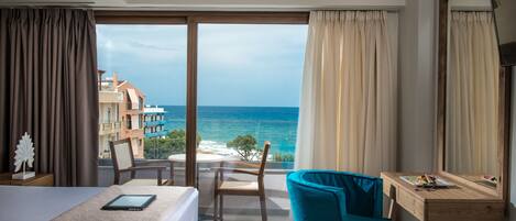 A hotel room with a bed, a desk, a chair, and a large window offering a view of the ocean and buildings.