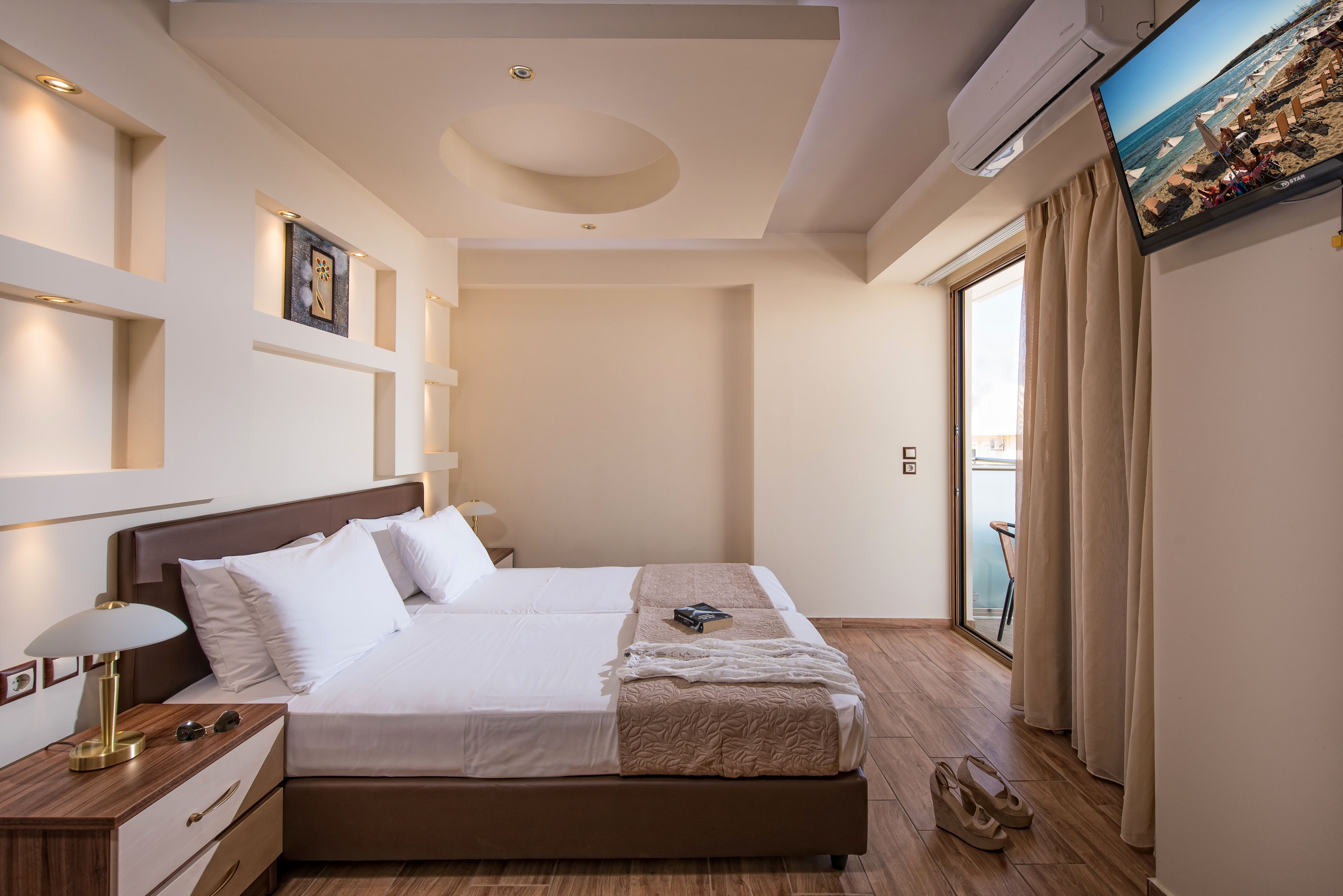 Un hotel moderno con una cama grande, una mesita de noche con lámpara, un televisor montado en la pared y vista al mar por la ventana.