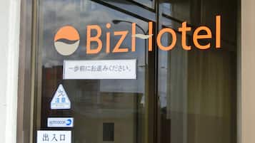 A glass door with the BizHotel logo, a pedestrian crossing sign, an auto door sign, and an exit sign.