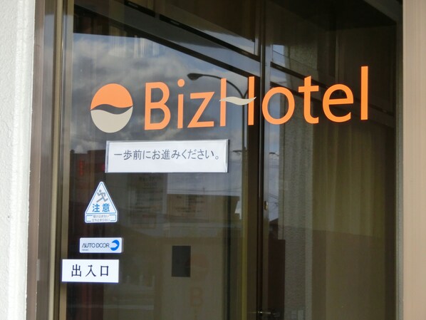 A glass door with the BizHotel logo, a pedestrian crossing sign, an auto door sign, and an exit sign.