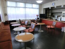 Habitación de hotel con sofá, varias sillas, una pequeña mesa, televisión, zona de cocina y un reloj en la pared.