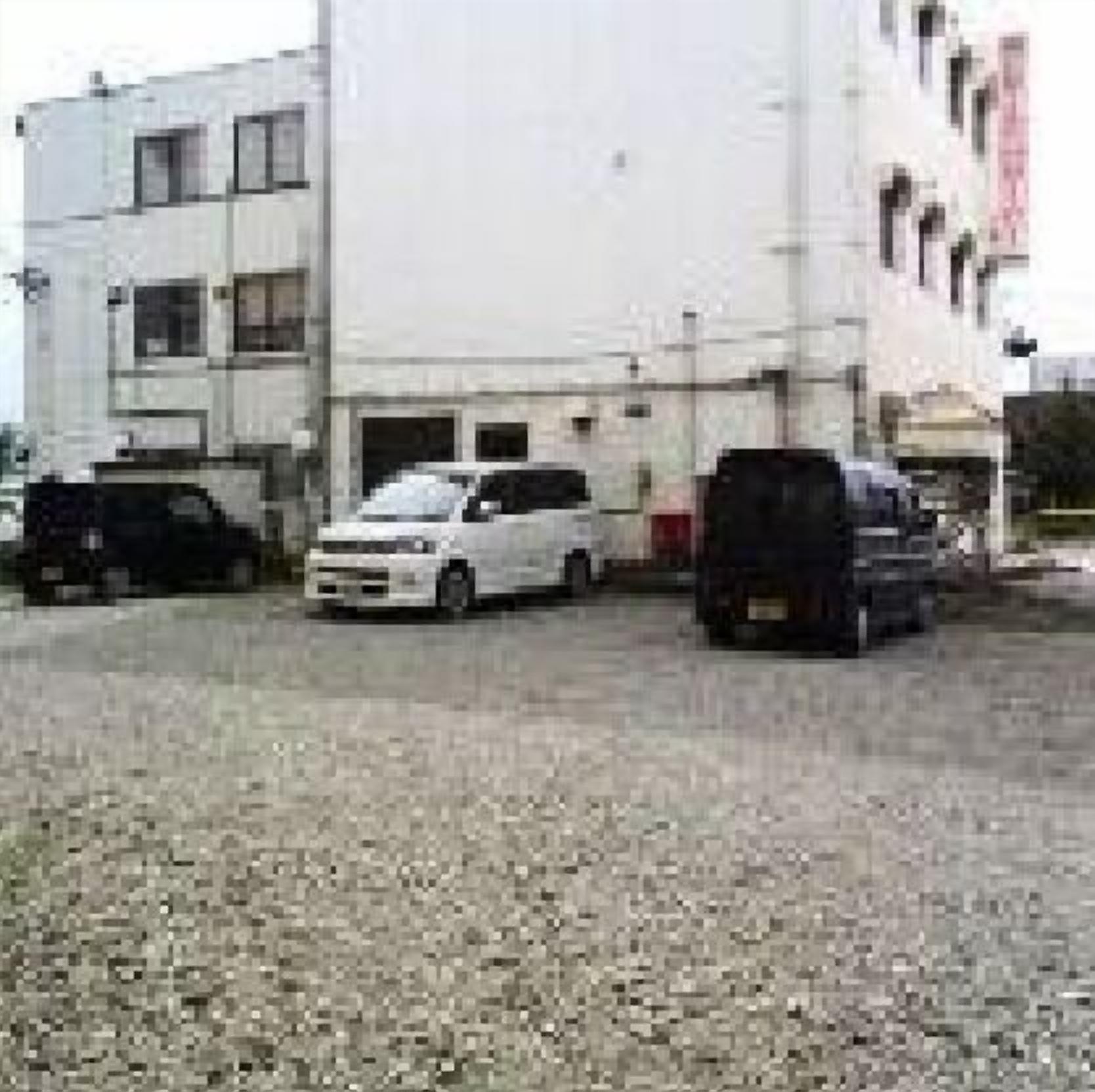 A parking lot with several cars, a building with multiple windows, and a gravel ground.