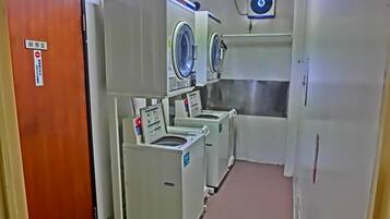 A laundry room with multiple washing machines and dryers, a wooden door, and a sign indicating it is a restricted area.