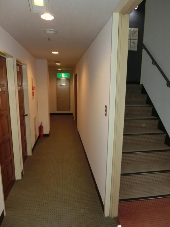 Un pasillo de hotel con pisos alfombrados, puertas de madera y una escalera con barandilla.