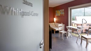 A modern spa room with a sauna area, a massage table, and a seating area with chairs and a table. - Hotel de Maretak (Dilsen-Stokkem)