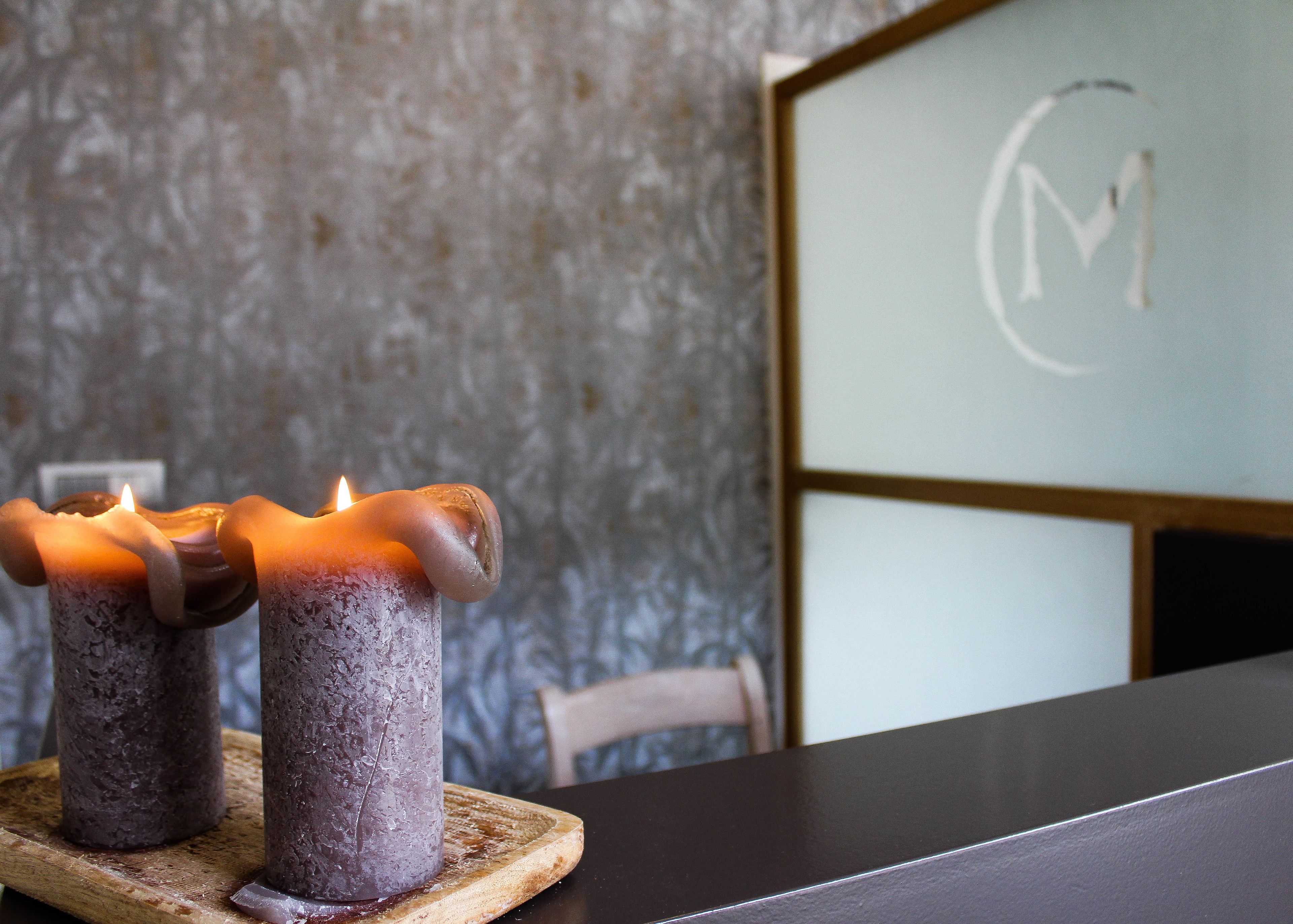 Two candles on a wooden coaster on a table.