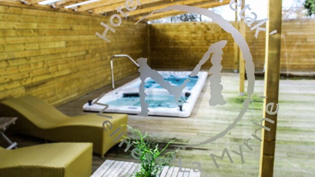 A wooden deck with a hot tub, lounge chairs, and a potted plant. - Hotel de Maretak (Dilsen-Stokkem)