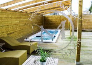 Eine Holzterrasse mit Whirlpool, Liegestühlen und einem Blumentopf.